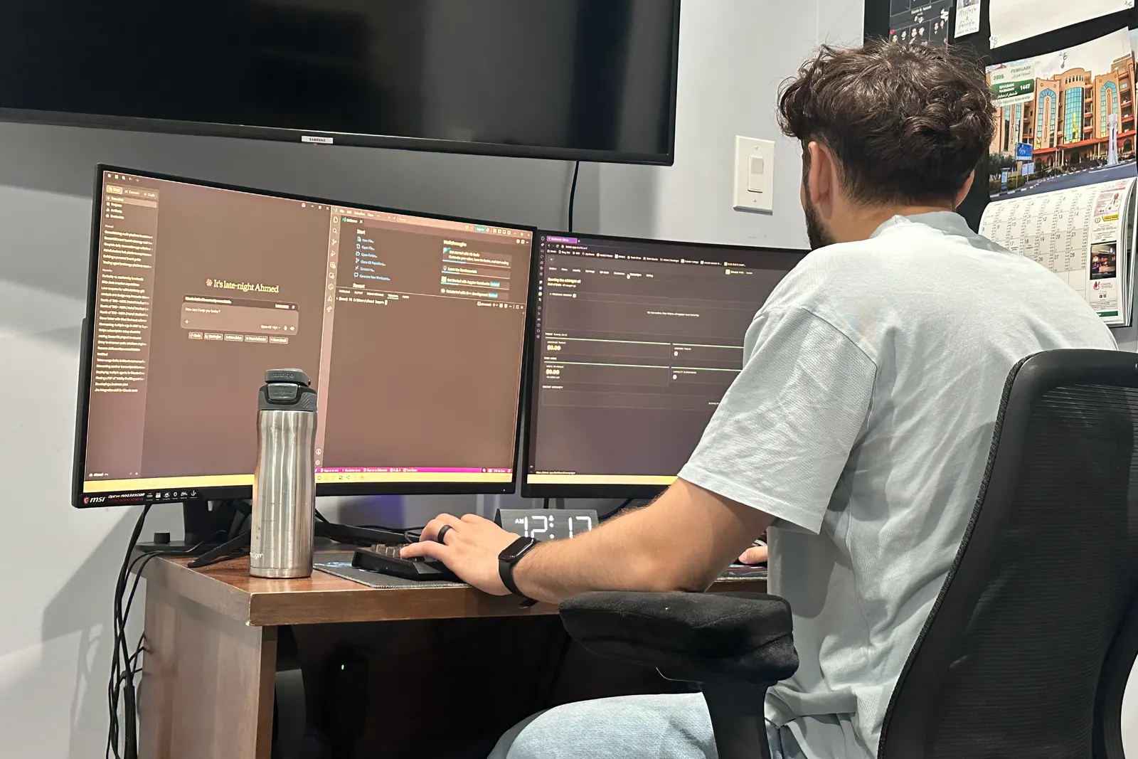 Ahmed Saqer at a three monitor desk setup, seen from behind, a code editor open on the centre screen.